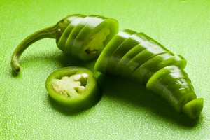 Photo of a sliced  green jalapeno pepper on green cutting board